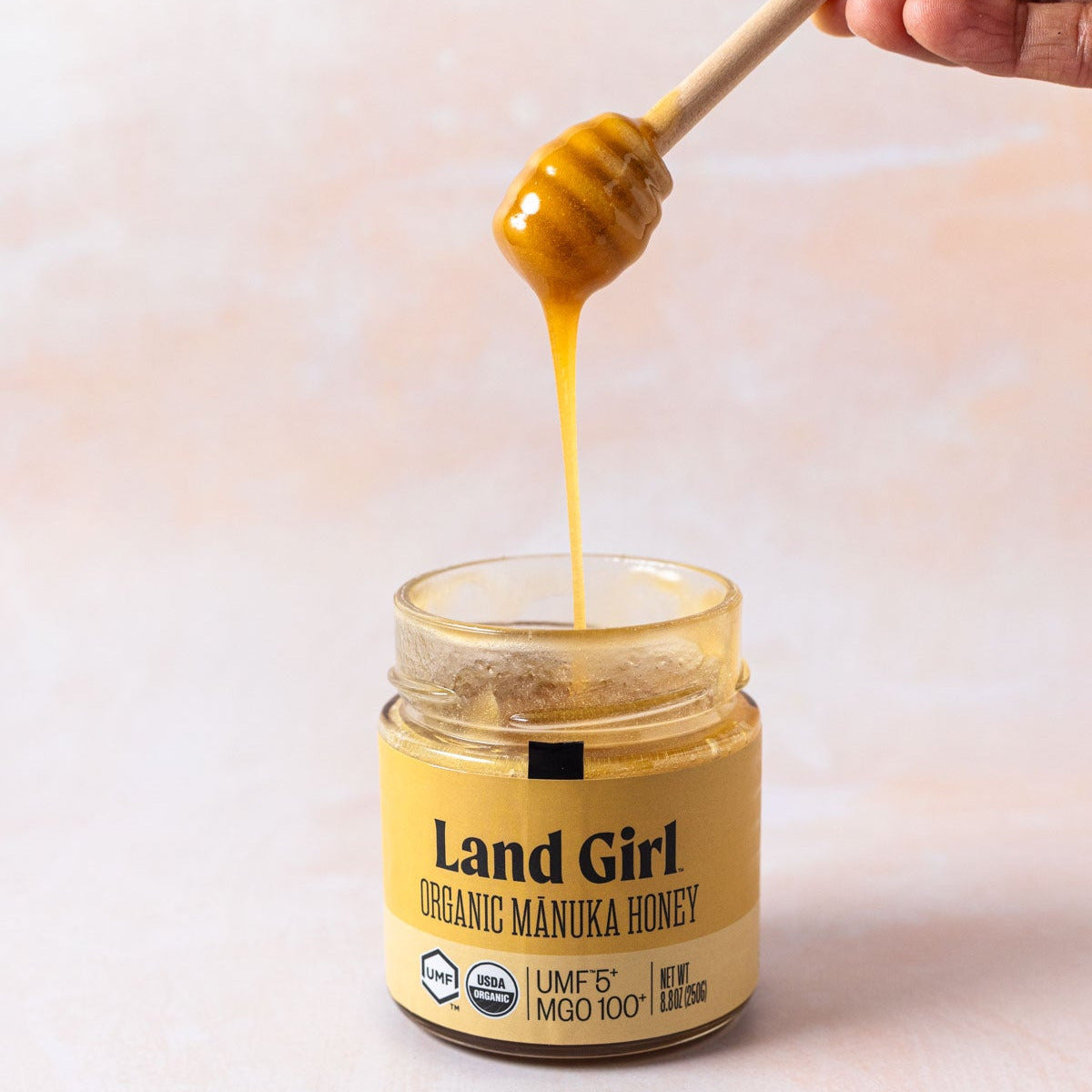 Jar of Land Girl Organic Manuka Honey with a honey dipper 