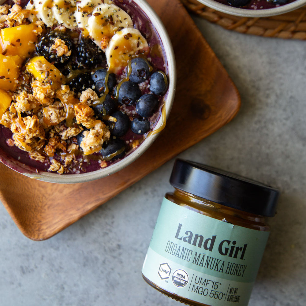 A acai bowl topped with granola, banana slices, blueberries, and organic māunka honey